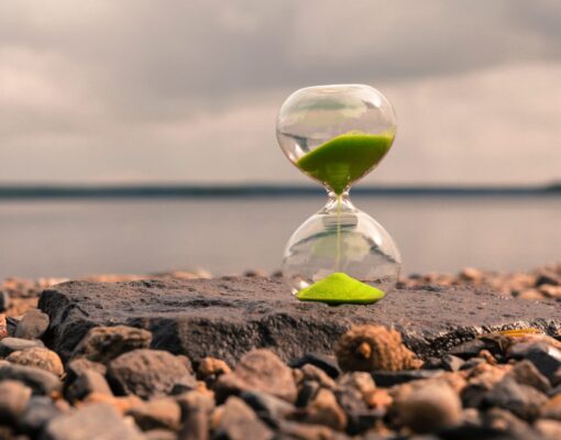Hourglass with green sand on the lake, stand on small stones. Time concept